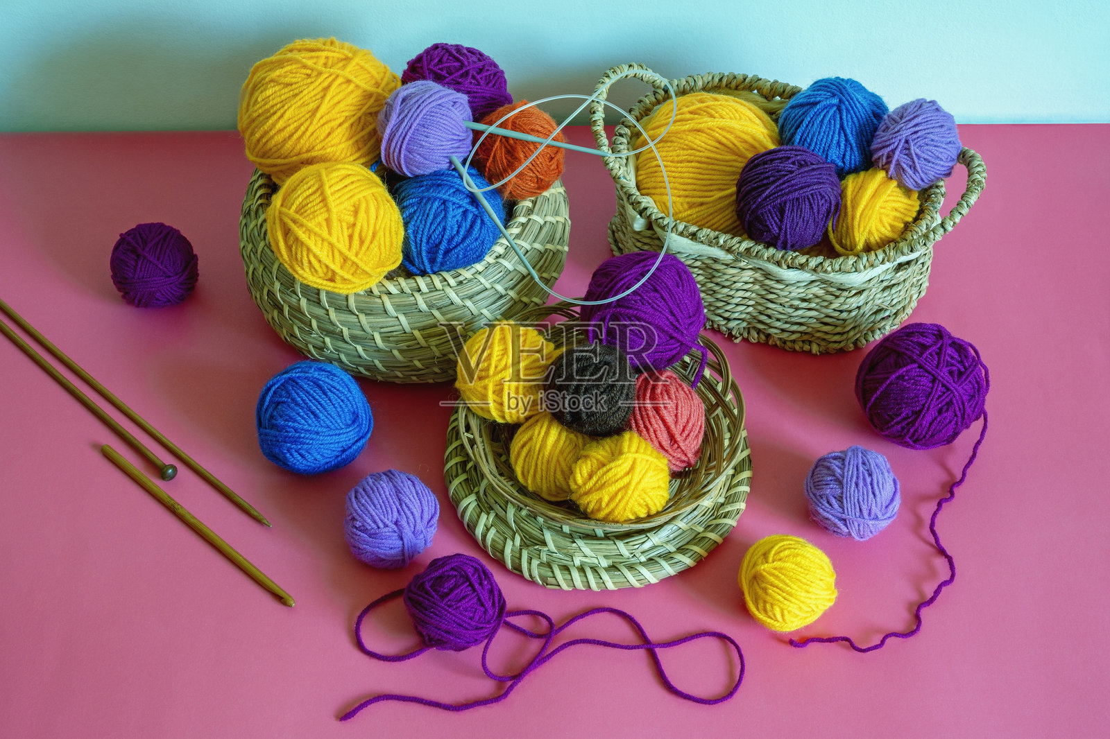 爱好与针织概念。粉红色背景上的小篮子里装着五颜六色的羊毛球和编织针照片摄影图片