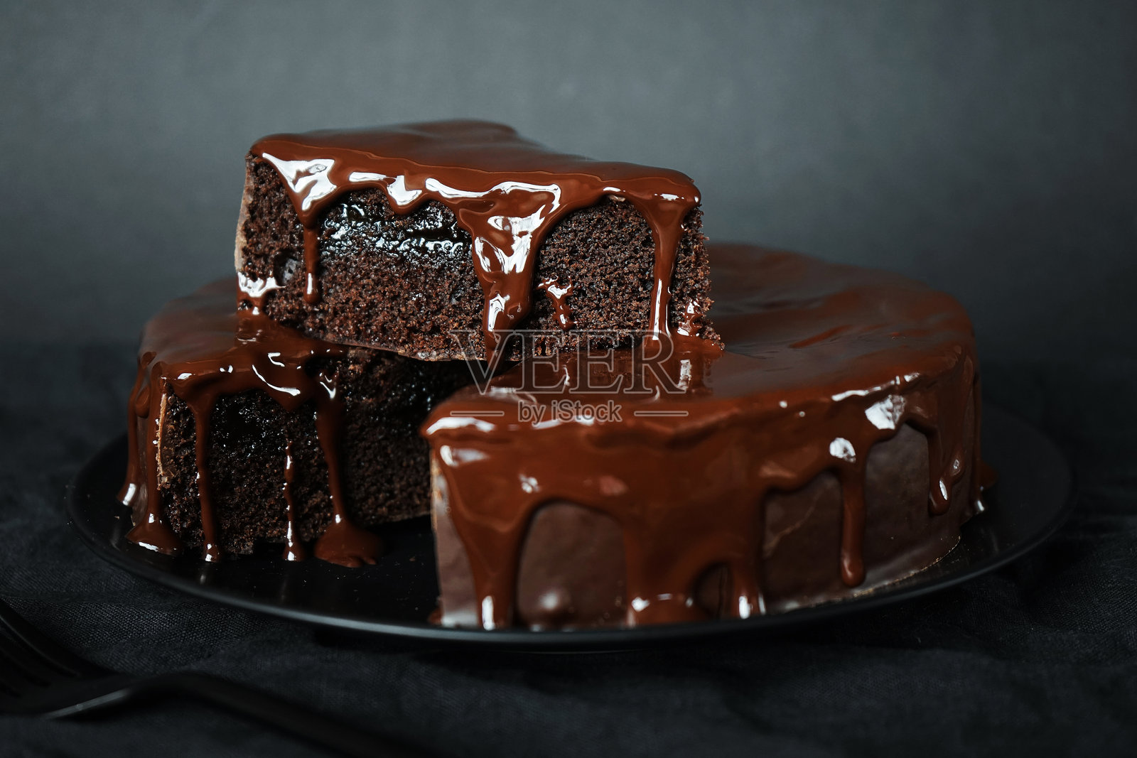 巧克力蛋糕和巧克力糖霜放在一个黑色盘子旁边的叉子照片摄影图片