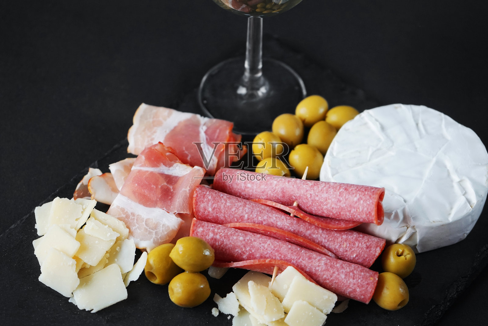布里干酪配意大利腊肠、培根、帕尔马干酪、橄榄，托盘上放一杯白葡萄酒照片摄影图片