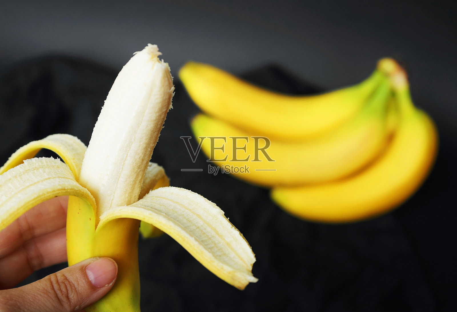 一个女人手里拿着去皮的香蕉，背景是一串成熟的香蕉照片摄影图片