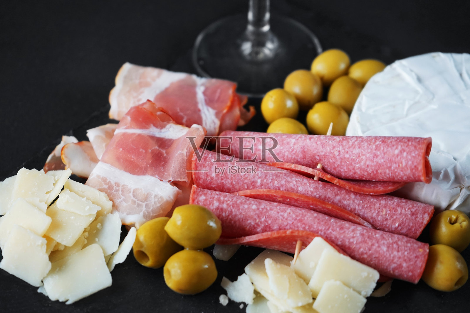 布里干酪配意大利腊肠、培根、帕尔马干酪、橄榄，托盘上放一杯白葡萄酒照片摄影图片