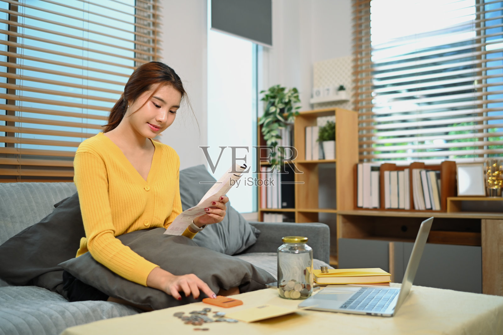 年轻女子坐在舒适的客厅里，享受着积攒下来的积蓄。规划未来的概念照片摄影图片