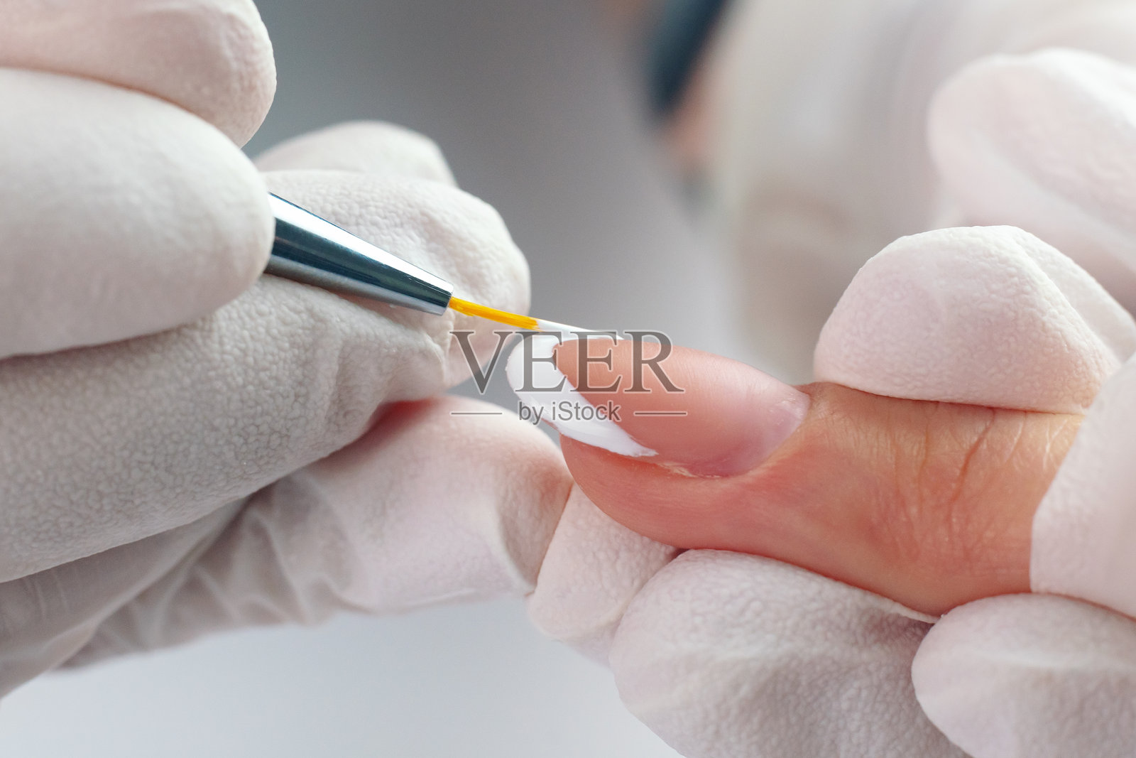 美甲师用细毛刷在指甲尖涂上白色指甲油，做法式美甲照片摄影图片