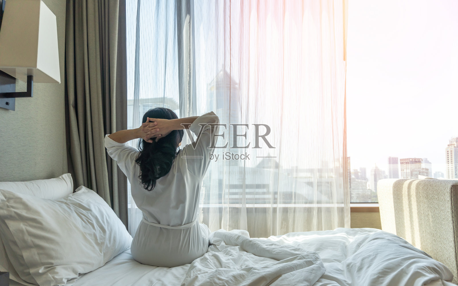 亚洲女性慵懒的一天在酒店放松，周末早上从床上睡个好觉醒来，在舒适的卧室里休息，享受快乐的工作与生活质量平衡的生活方式照片摄影图片