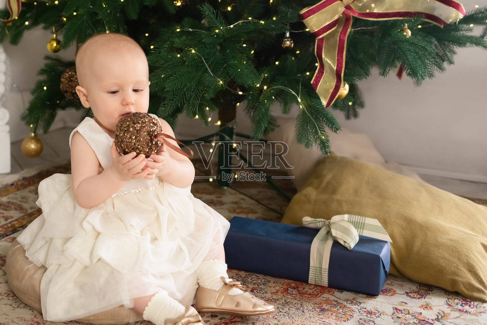 在为新年装饰的客厅里，一个穿着漂亮的白色连衣裙的小女孩坐在圣诞树旁边照片摄影图片