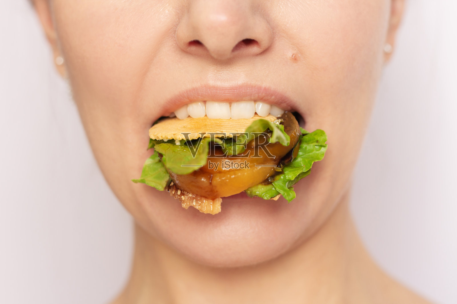 一个年轻女子的脸部特写，嘴里叼着一个健康的蔬菜三明治照片摄影图片
