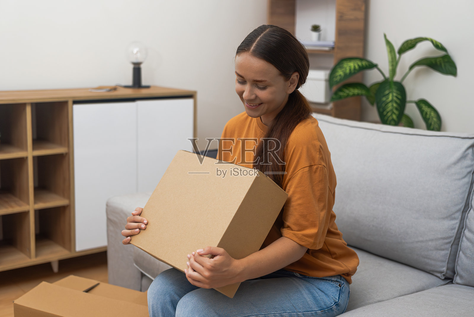 一个女人拿着一个纸板箱，象征着收到她在网上购物的满意。照片摄影图片