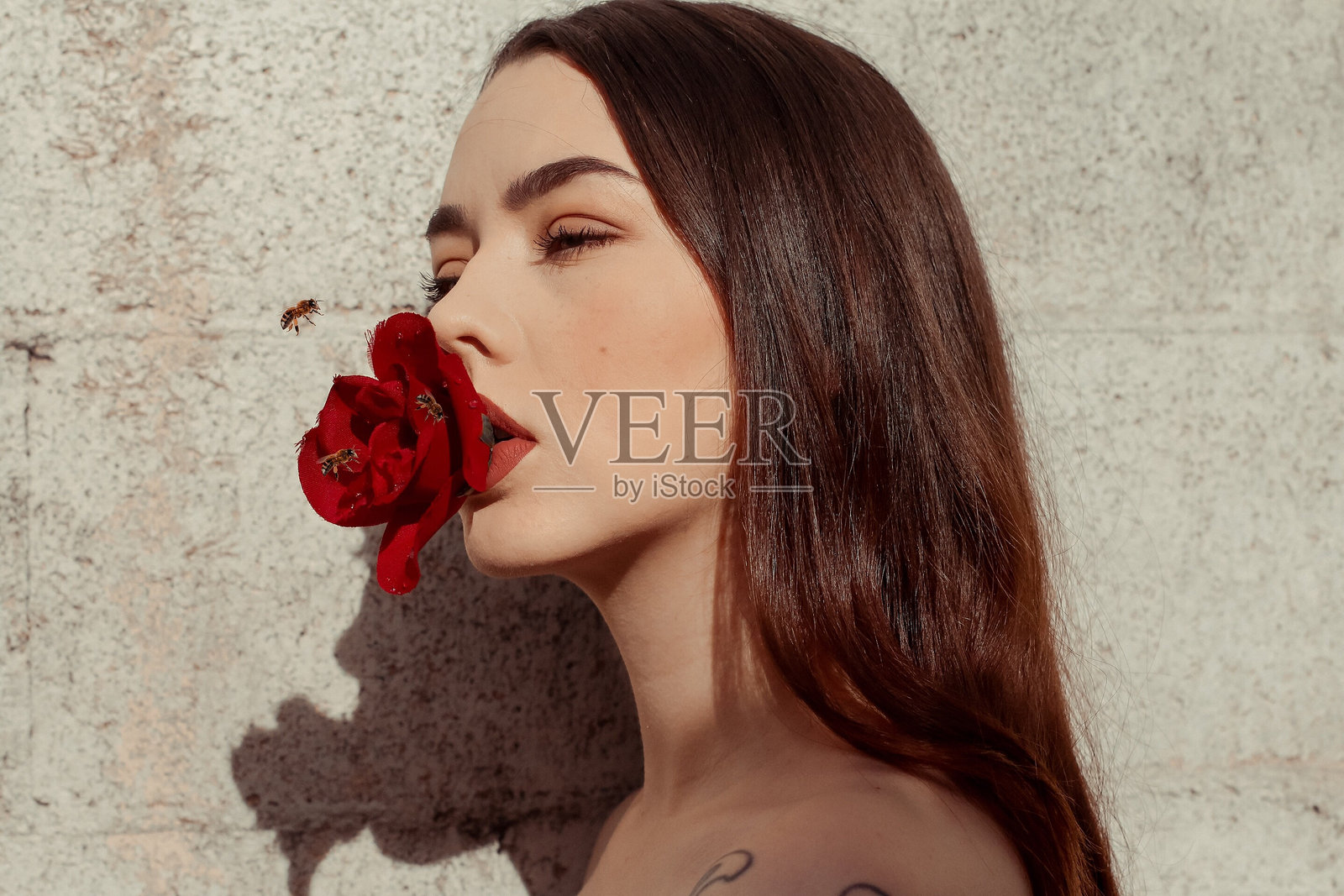 年轻女子手持玫瑰靠墙的特写照片摄影图片