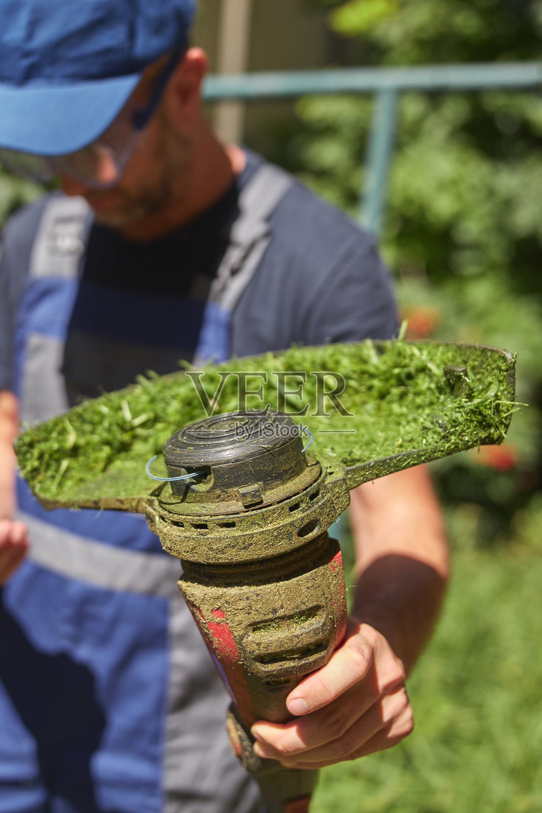 园丁用草修剪机修剪建筑物周围杂草丛生的草和杂草，并更换磨损的绳子。照片摄影图片