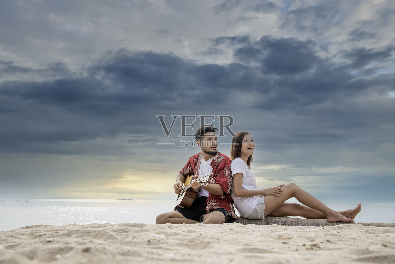 一对恋人弹吉他，一起唱歌，在热带的夏日沙滩上约会。两人一起约会的浪漫时刻伴随着幸福的浪漫。女友男友在沙滩上吉他手爱好海边照片摄影图片