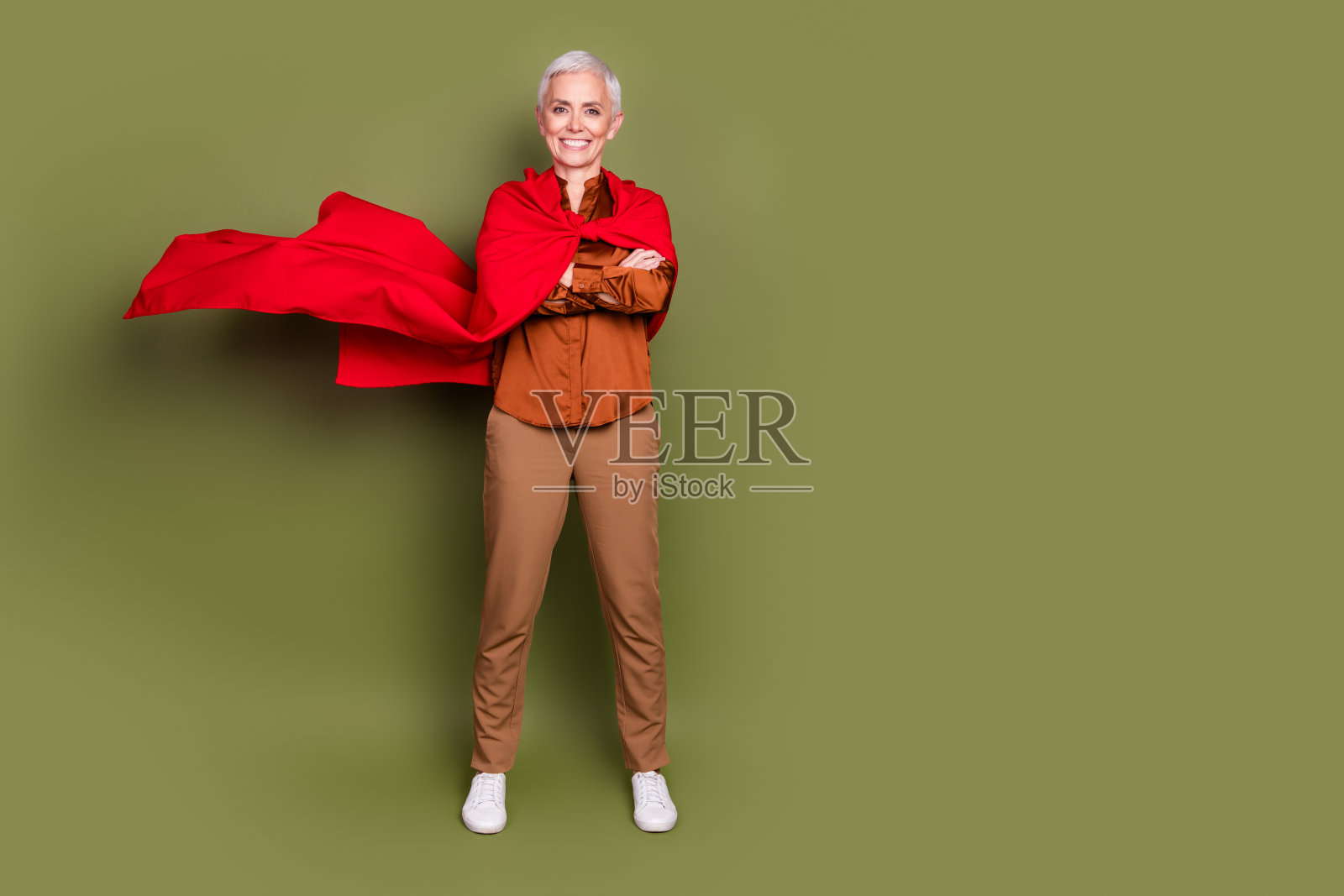 迷人的资深女性的全身照片，双手交叉，自信的超级英雄穿着棕色正装，在卡其色的背景上孤立照片摄影图片