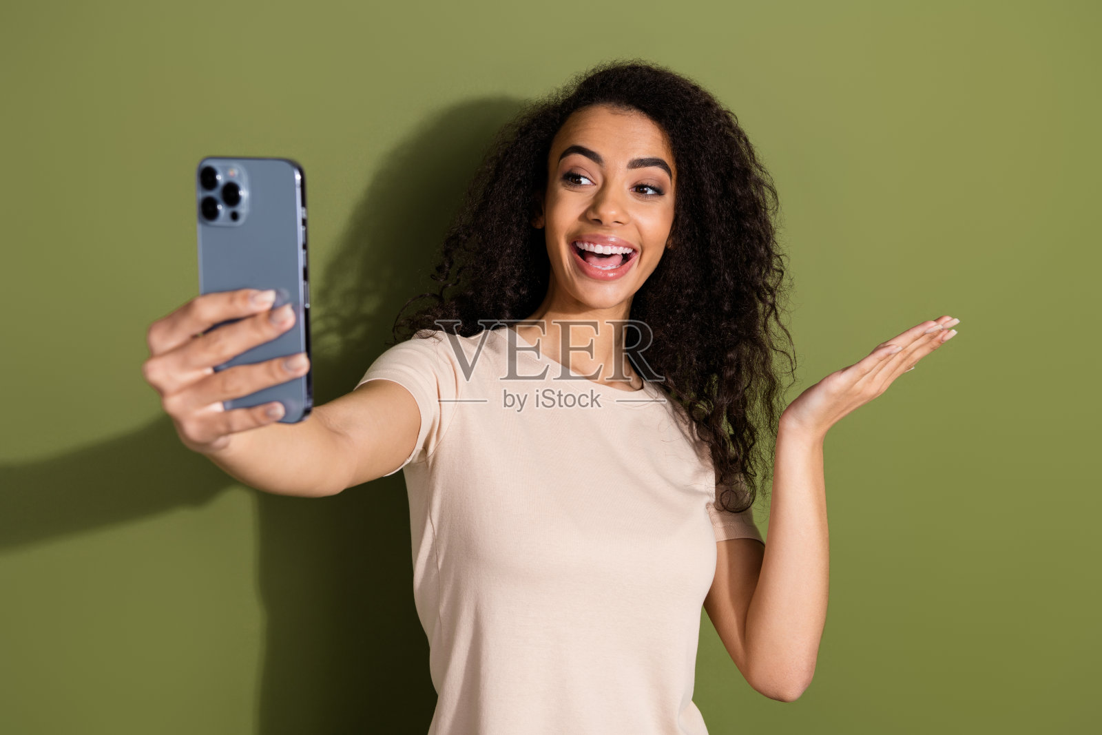 乐观的女孩穿着米色t恤的照片，自拍智能手机手掌握着物体，在卡其色背景上孤立的空白空间照片摄影图片