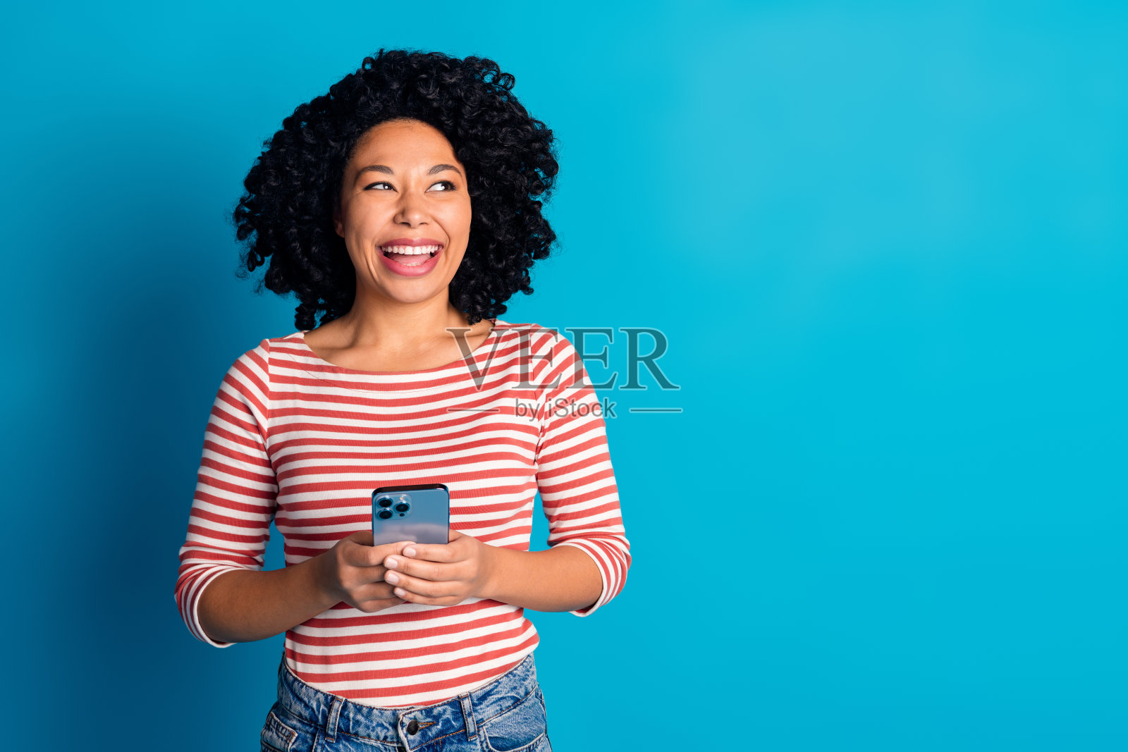 照片正面迷人的女孩穿着时髦的衣服，抱着现代的小玩意，在蓝色的背景上孤立的空间照片摄影图片