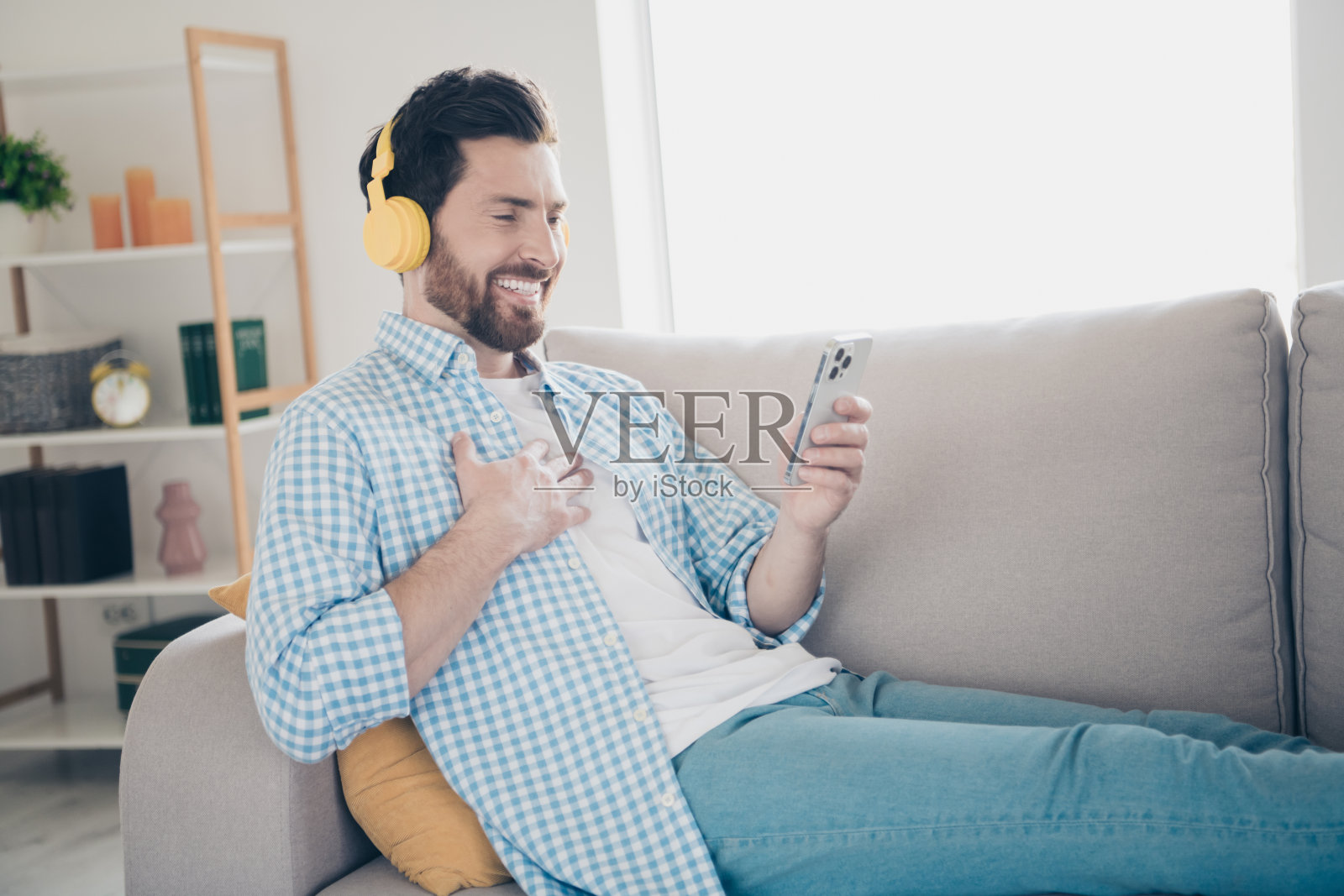 开朗的大胡子孤独的成熟成年男子躺在舒适的沙发上，戴着耳机听音乐，和网友聊天照片摄影图片