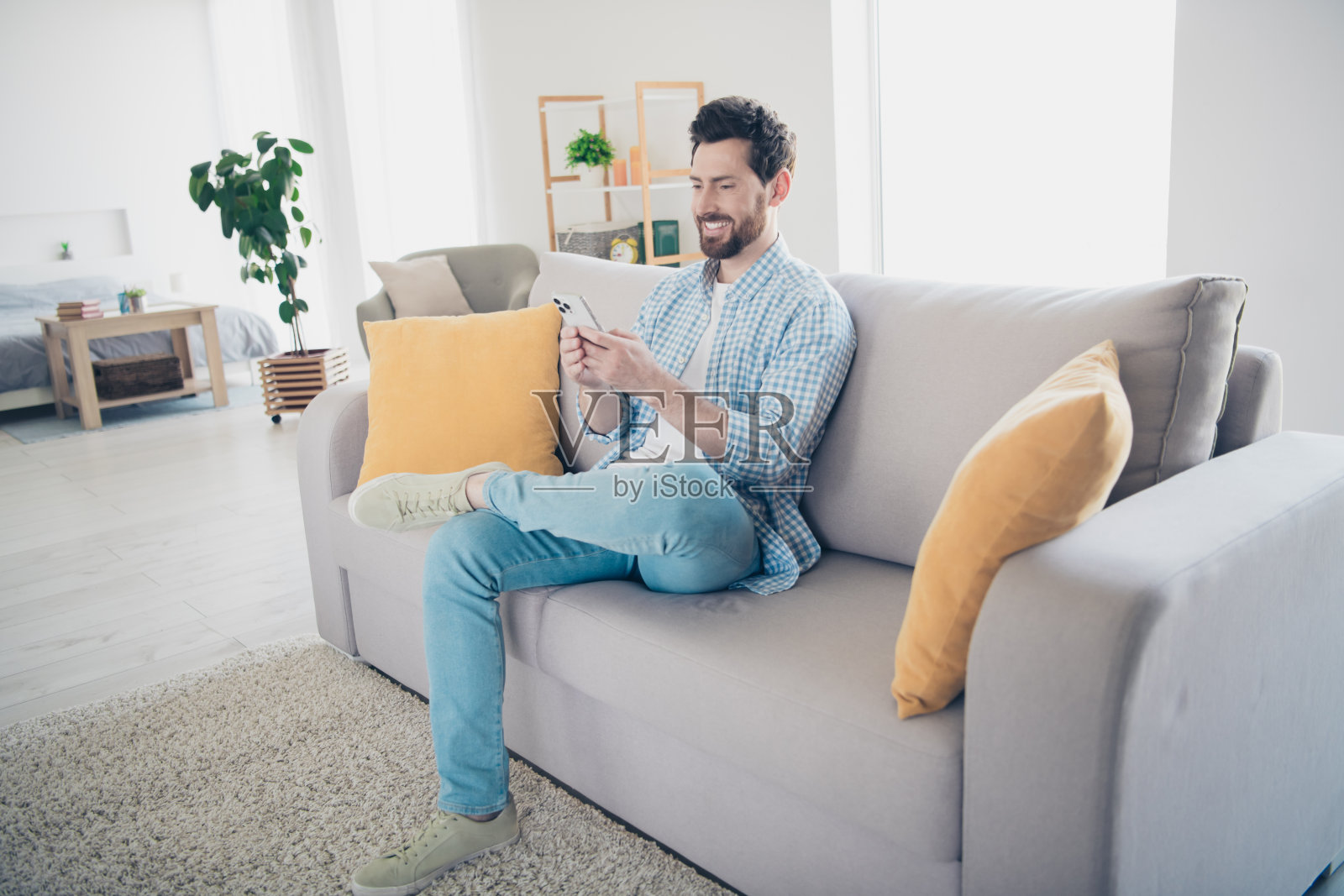 英俊的大胡子的成年男子独自呆在家里的客厅与巨大的沙发阁楼设计和浏览新闻电话的照片照片摄影图片