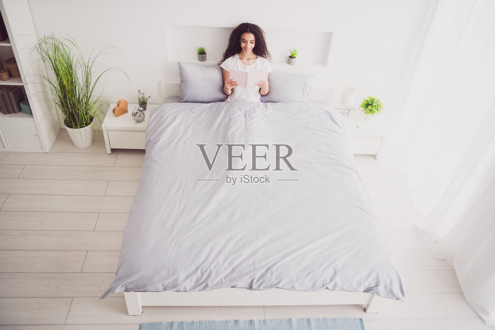 年轻迷人的女人的全身照片躺在床上阅读穿着时尚的睡衣柔软舒适的卧室白色的房间内部照片摄影图片