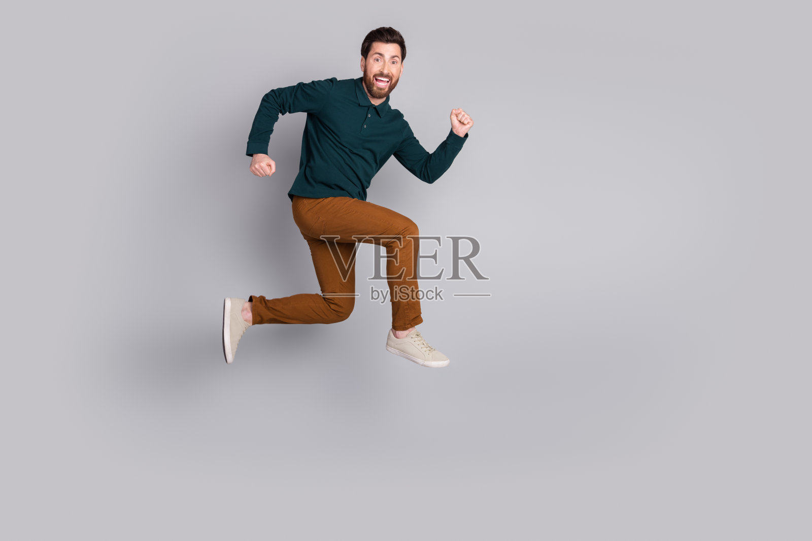 照片中，疯狂有趣的积极向上的男人穿着时髦的绿色衣服跑得飞快，空白的空间孤立在灰色的背景上照片摄影图片