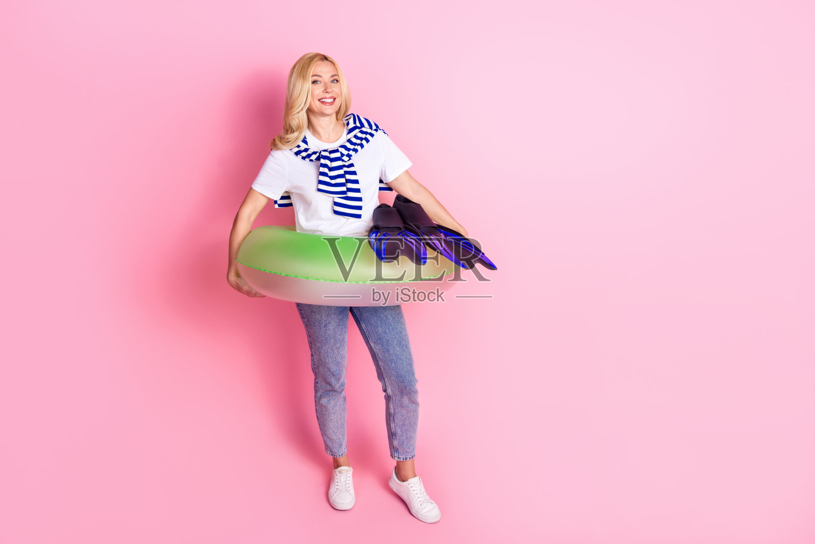 漂亮的年轻女性充气环形脚蹼的全尺寸照片，穿着时髦的白色衣服，孤立在粉红色的背景上照片摄影图片