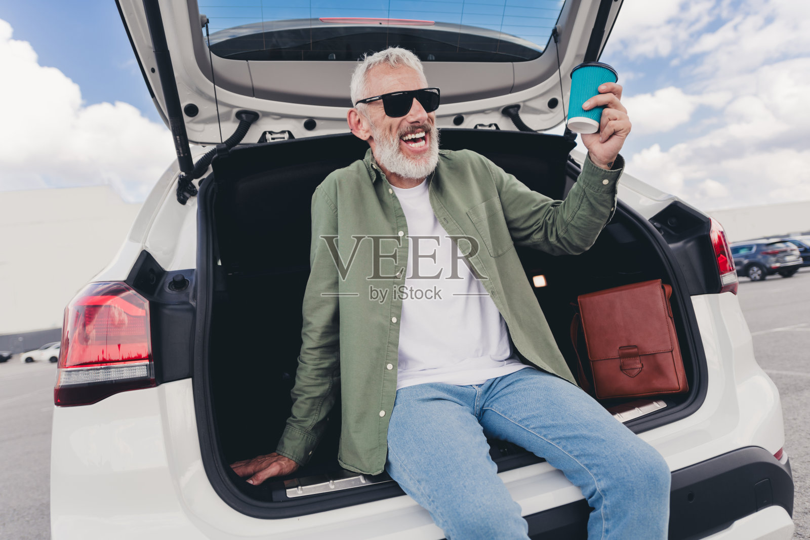迷人有趣的退休男子穿着卡其布衬衫坐在汽车后备箱享受咖啡到户外城市街道的照片照片摄影图片