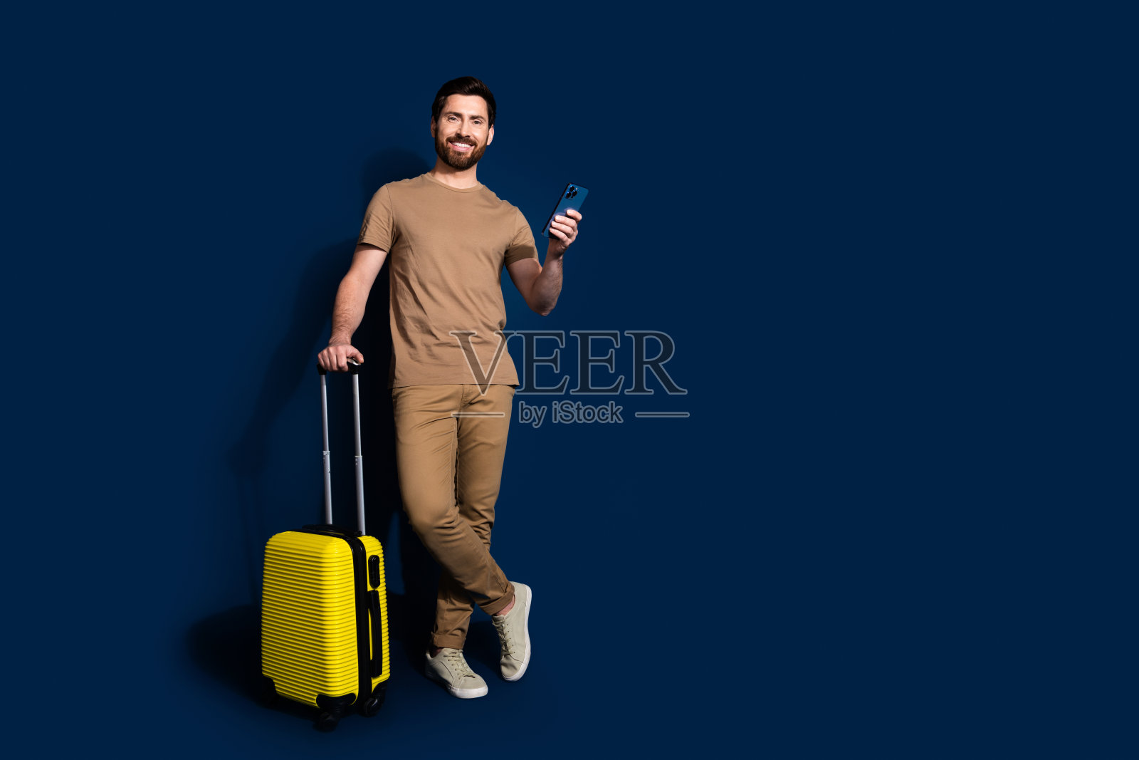 成熟年龄的深色胡子滑稽男子的照片肖像用智能手机买机票孤立的深蓝色背景照片摄影图片