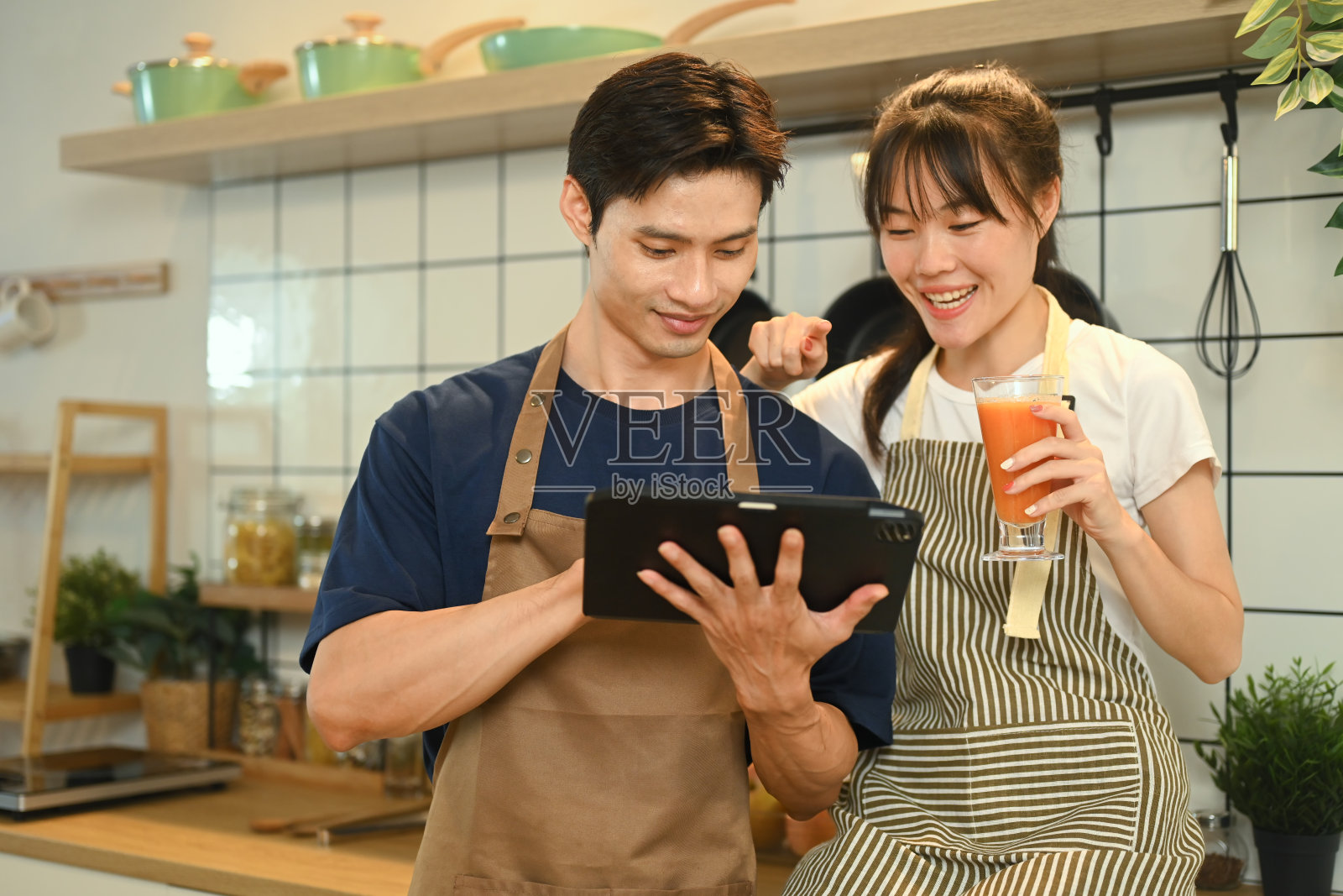 幸福的年轻夫妇在网上寻找食谱或在平板电脑上的烹饪教程，在厨房做饭照片摄影图片