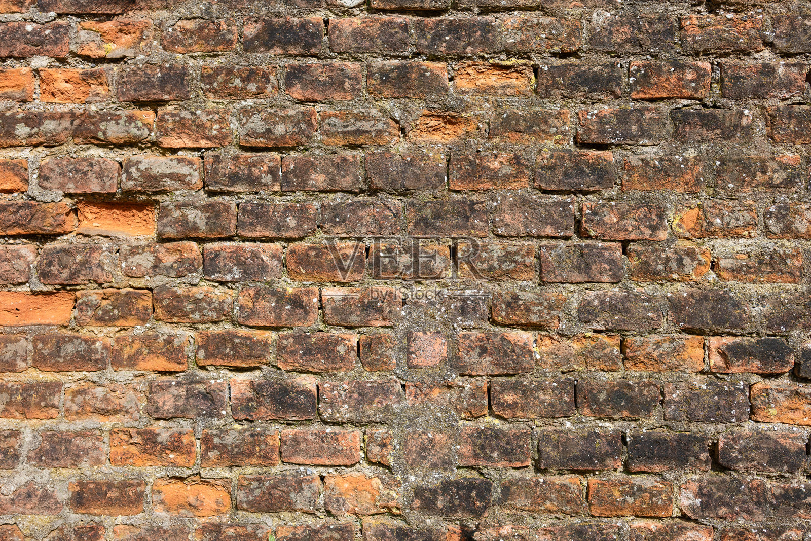 一堵老砖墙的特写，上面有深浅不一的红色和棕色砖块，显示出风化和苔藓生长的迹象。砖块的纹理和不规则突出了时间的流逝照片摄影图片