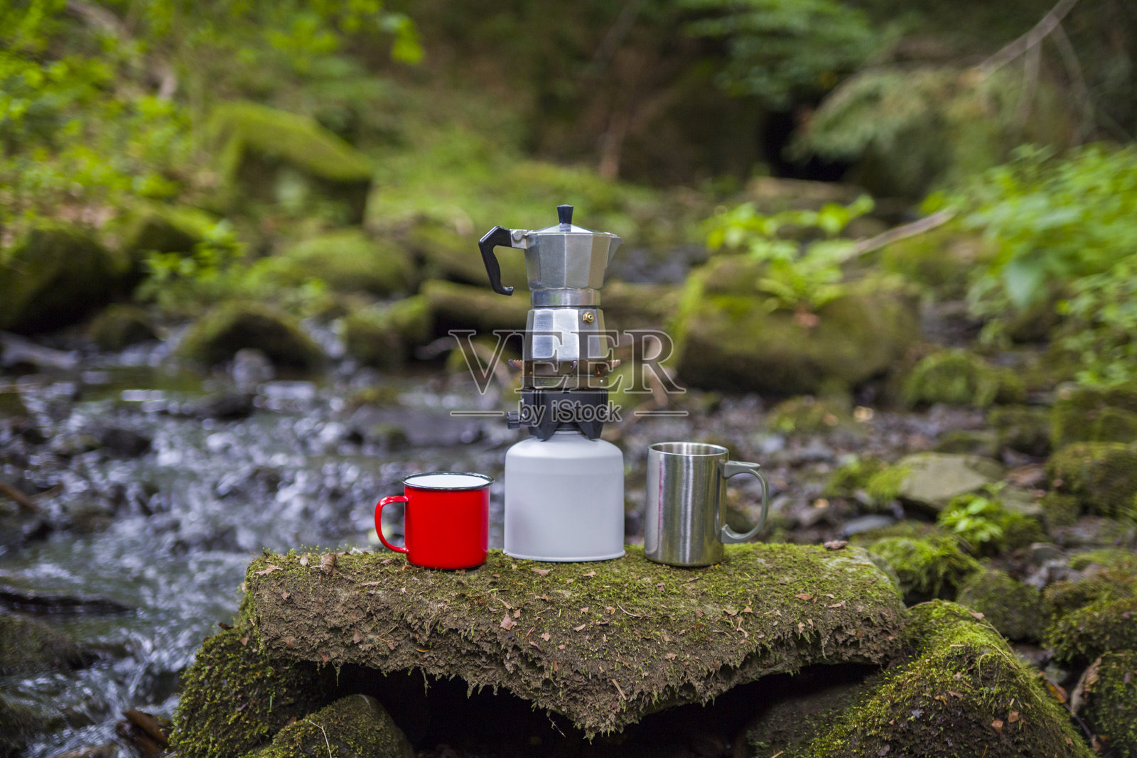 咖啡壶和金属杯放在一块大石头上，背景是一条山河。石板上的咖啡壶映衬着模糊的自然背景。照片摄影图片