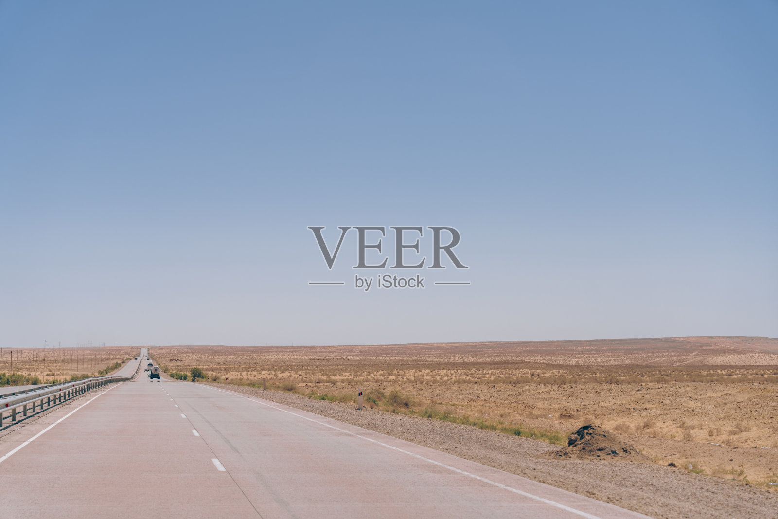 一条又长又空的路，头顶蓝天。道路两旁长着高高的草，有一辆汽车在路上行驶照片摄影图片