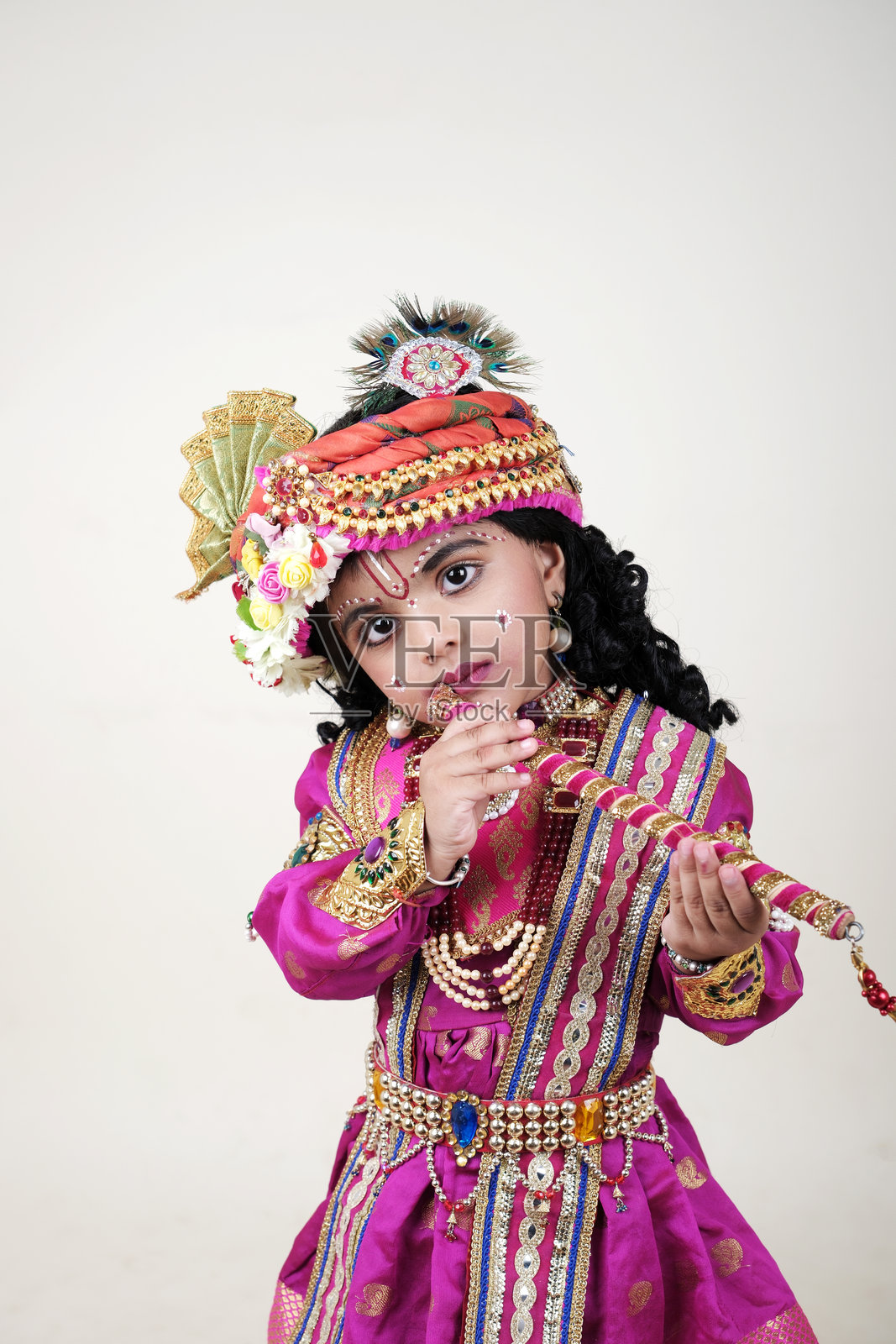 一个年轻的印度孩子，穿着传统服装，用神圣的触摸来庆祝Janmashtami，带着天真的喜悦吹着长笛。照片摄影图片