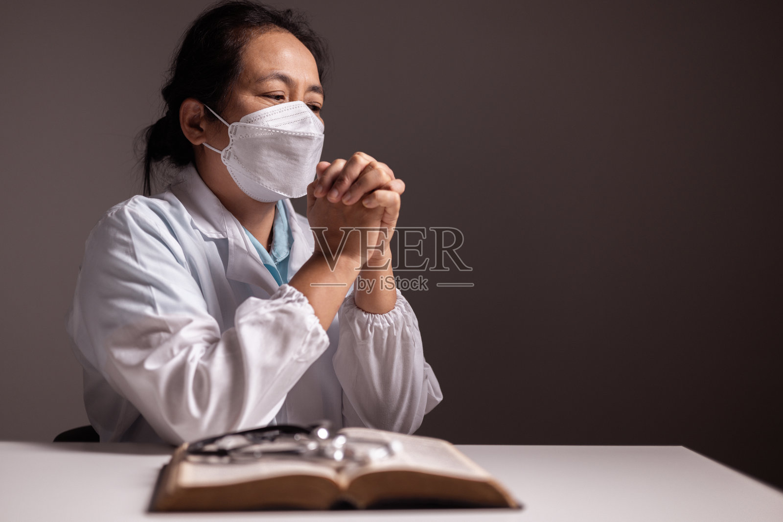 一名妇女双手合十祈祷，她在医院或诊所面对疾病时，相信医生和医疗专业人员的照顾，相信医疗保健的力量。医生,疾病。照片摄影图片