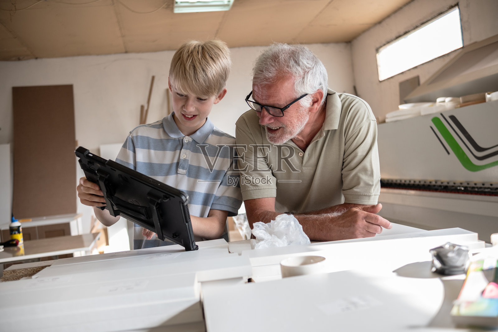 一位祖父在他的木匠作坊里教他的孙子如何修理家具。照片摄影图片