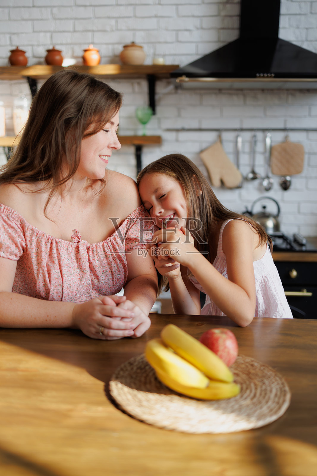 微笑的女人看着女儿在厨房里的水果照片摄影图片