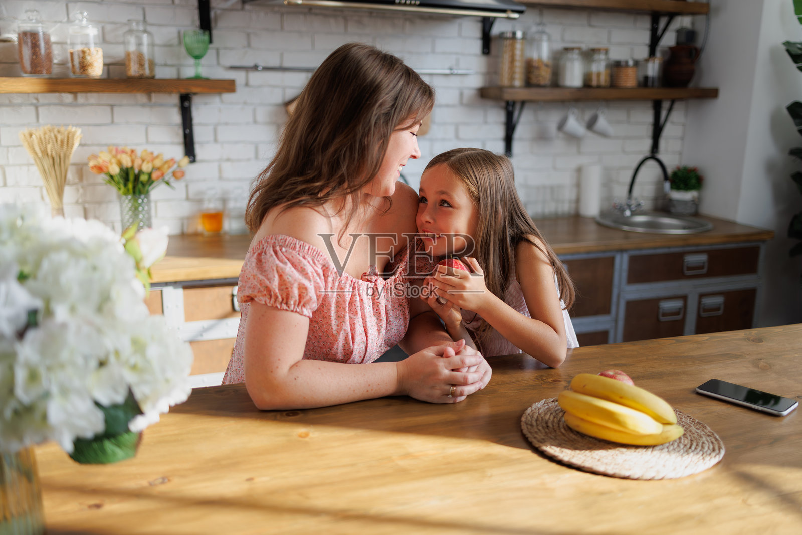 在家里的厨房里，女人抱着带着水果微笑的女儿照片摄影图片