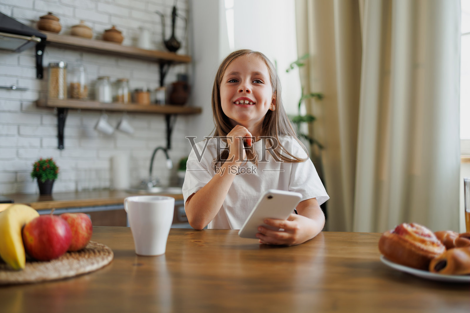 肯定有孩子在厨房里拿着手机靠近面包和水果照片摄影图片