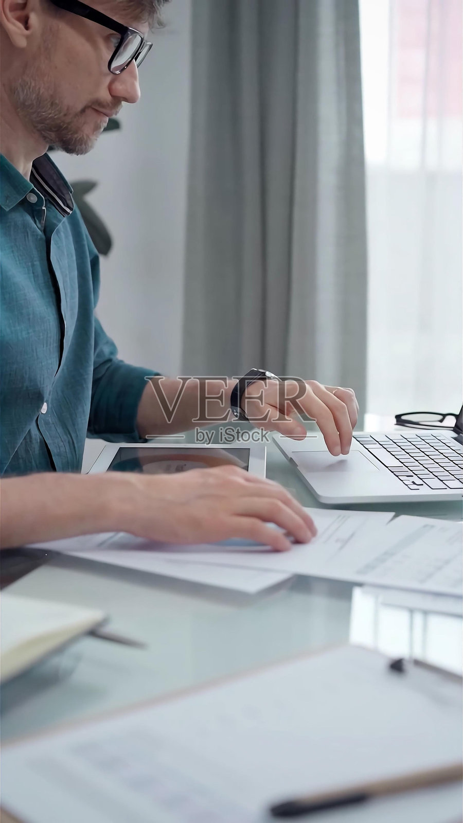 穿着绿色衬衫，戴着眼镜的商人正在用笔记本电脑和数据分析图表工作。垂直商业肖像照片摄影图片