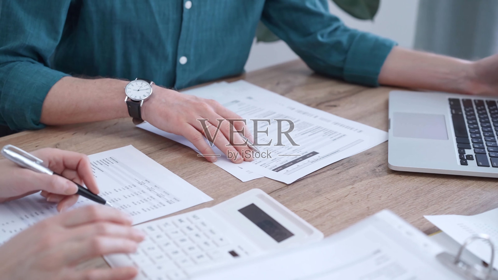 穿着绿色衬衫的审核员正在审阅文件，并与同事一起使用笔记本电脑。商务人士专业人士分析财务文件。财务、审计和税务照片摄影图片