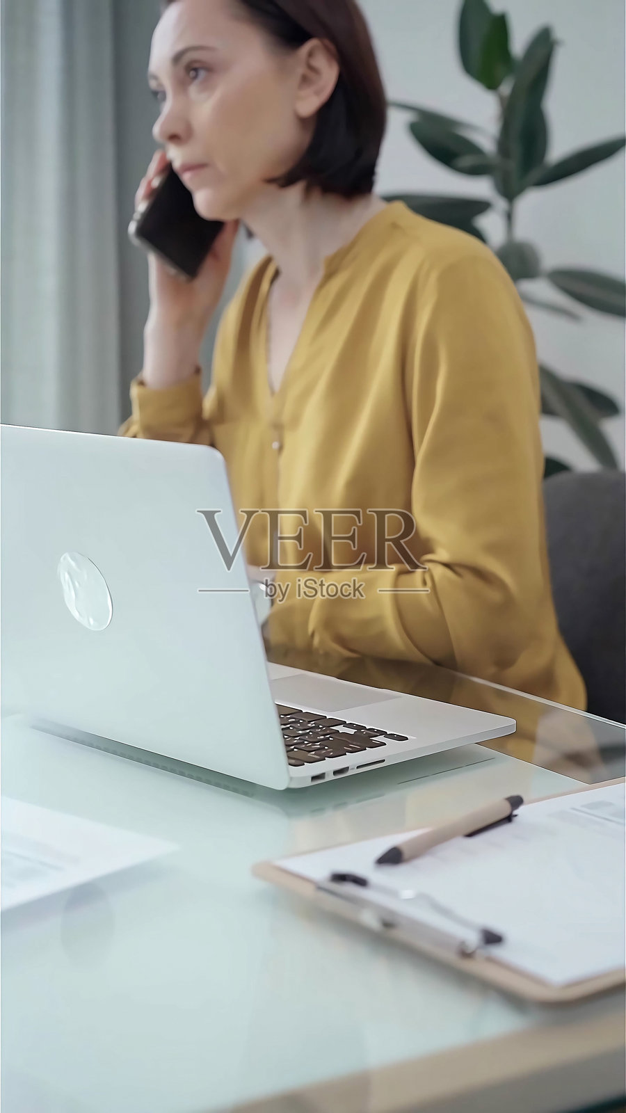 年轻的职业女性正在办公室里用智能手机聊天。黄衬衫正传给成年女商人。经营理念照片摄影图片