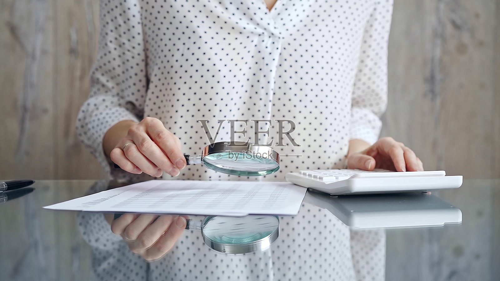 女审计员在她的办公桌旁用放大镜和计算器分析财务文件，她穿着带圆点花纹的白衬衫。商务人士概念照片摄影图片