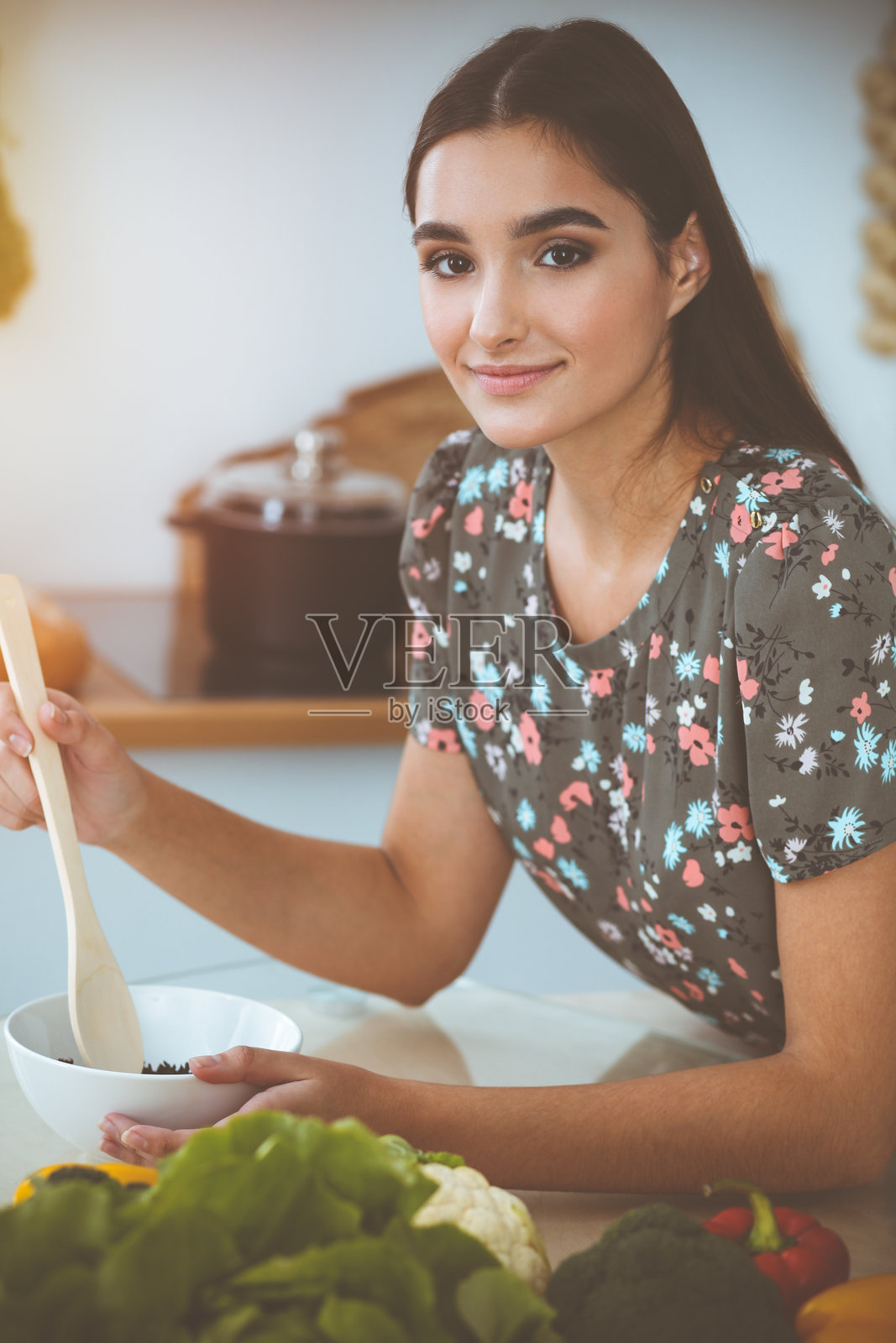 在阳光明媚的厨房里，一位年轻迷人的黑发女子坐在餐桌旁，品尝着一道美味的沙拉新配方照片摄影图片