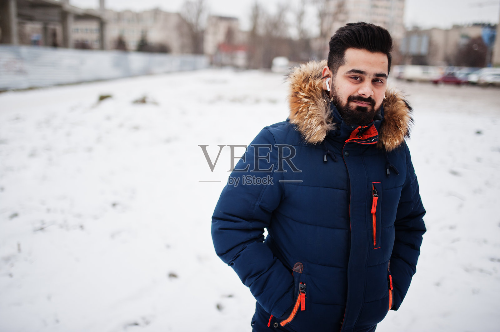 有胡子的印第安人在寒冷的冬天穿夹克。耳塞移动耳机。照片摄影图片