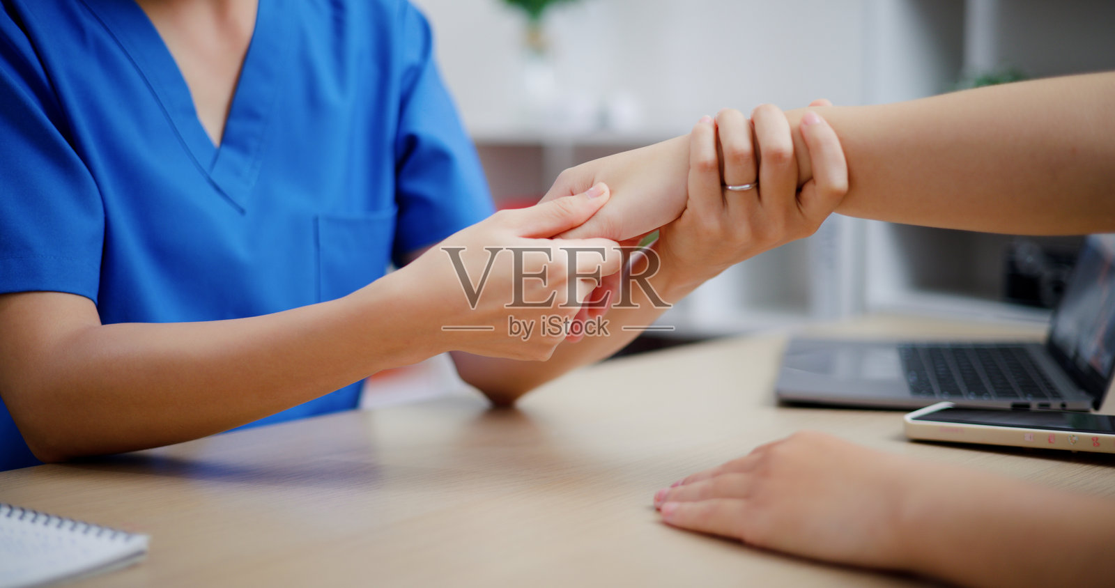 图为，在检查室里，身穿工作服的亚洲女医务人员正在为患者的手腕进行物理治疗。照片摄影图片