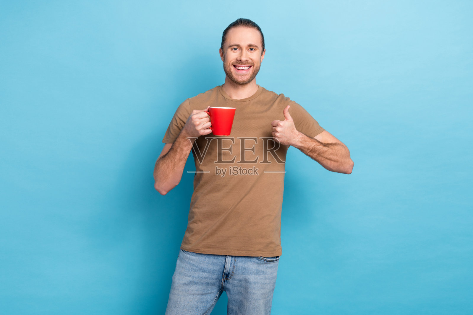 漂亮积极的人的肖像拿着新鲜的热咖啡杯显示拇指向上孤立在蓝色背景照片摄影图片