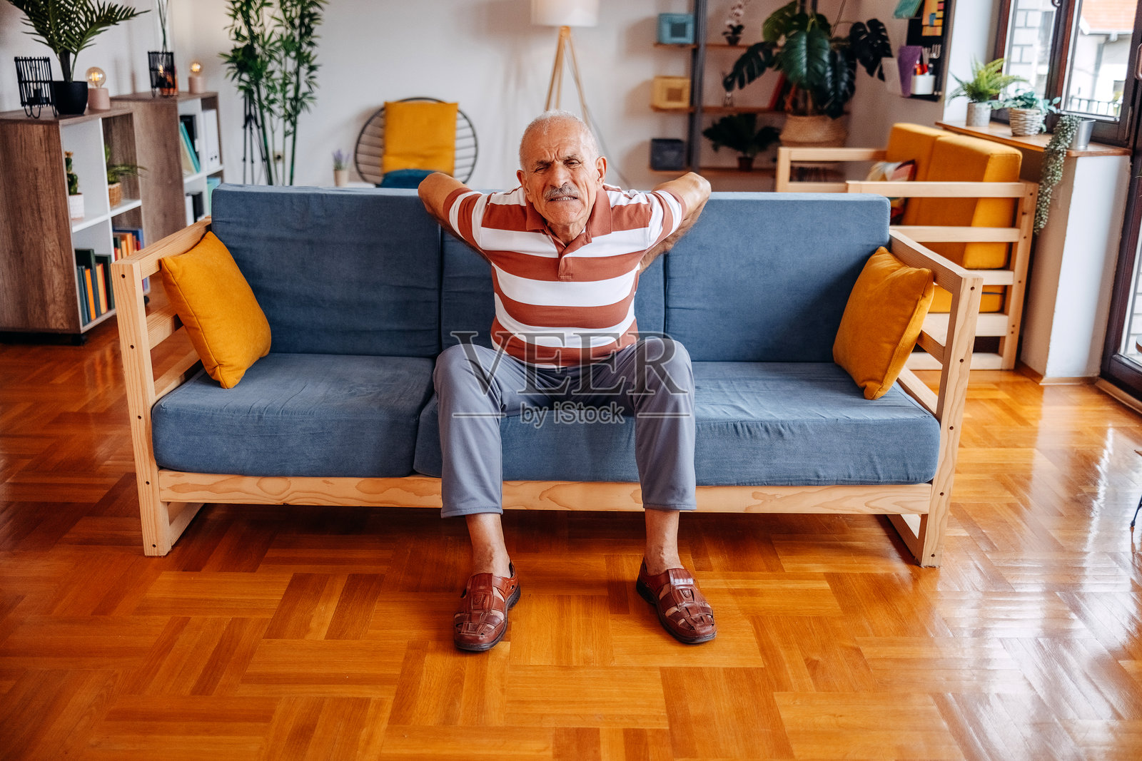 老人坐在家里客厅的沙发上感到疼痛照片摄影图片