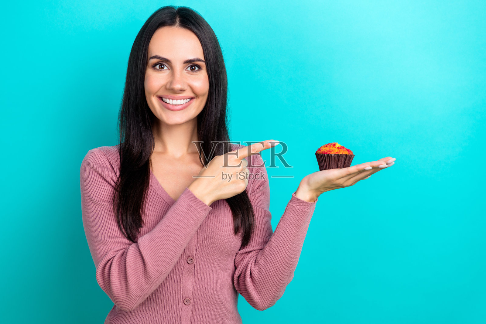 漂亮开朗的女士的照片，露齿微笑，直接手指手臂拿松饼甜点孤立在蓝绿色的背景照片摄影图片