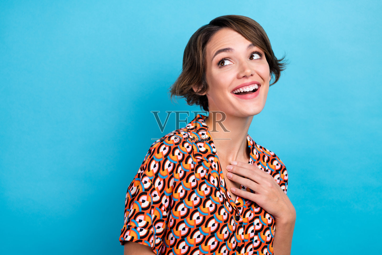 照片中甜美梦幻的女士穿着印花衬衫微笑着回头看空旷孤立的蓝色背景照片摄影图片