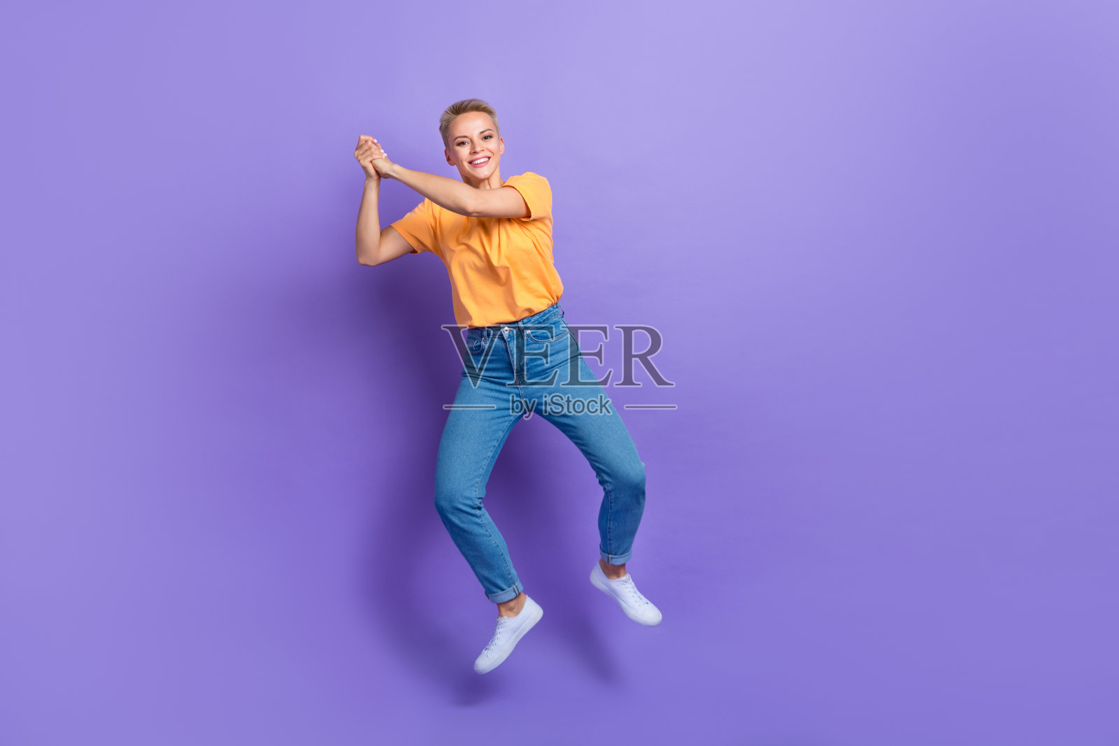 友好俏皮的女孩穿着牛仔裤白色运动鞋手持想象的网球拍孤立的紫罗兰色背景的全长照片照片摄影图片