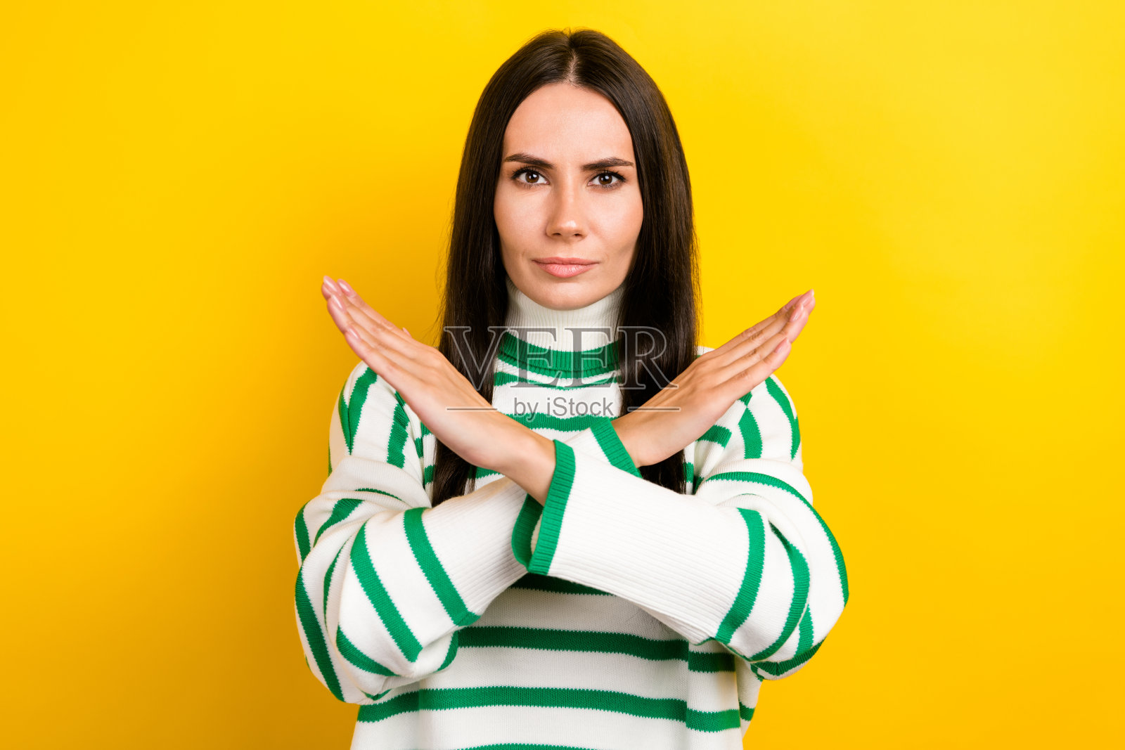 照片中，严肃自信的女士穿着条纹套头衫，双臂交叉，要求停止孤立的黄色背景照片摄影图片
