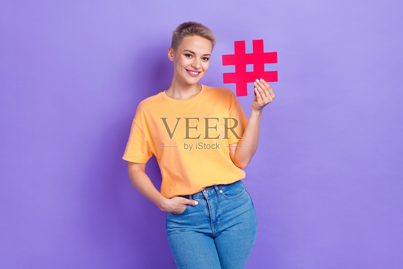 好心情的好女孩，短发，穿着黄色t恤，手臂放在口袋里，孤立的紫色背景照片摄影图片