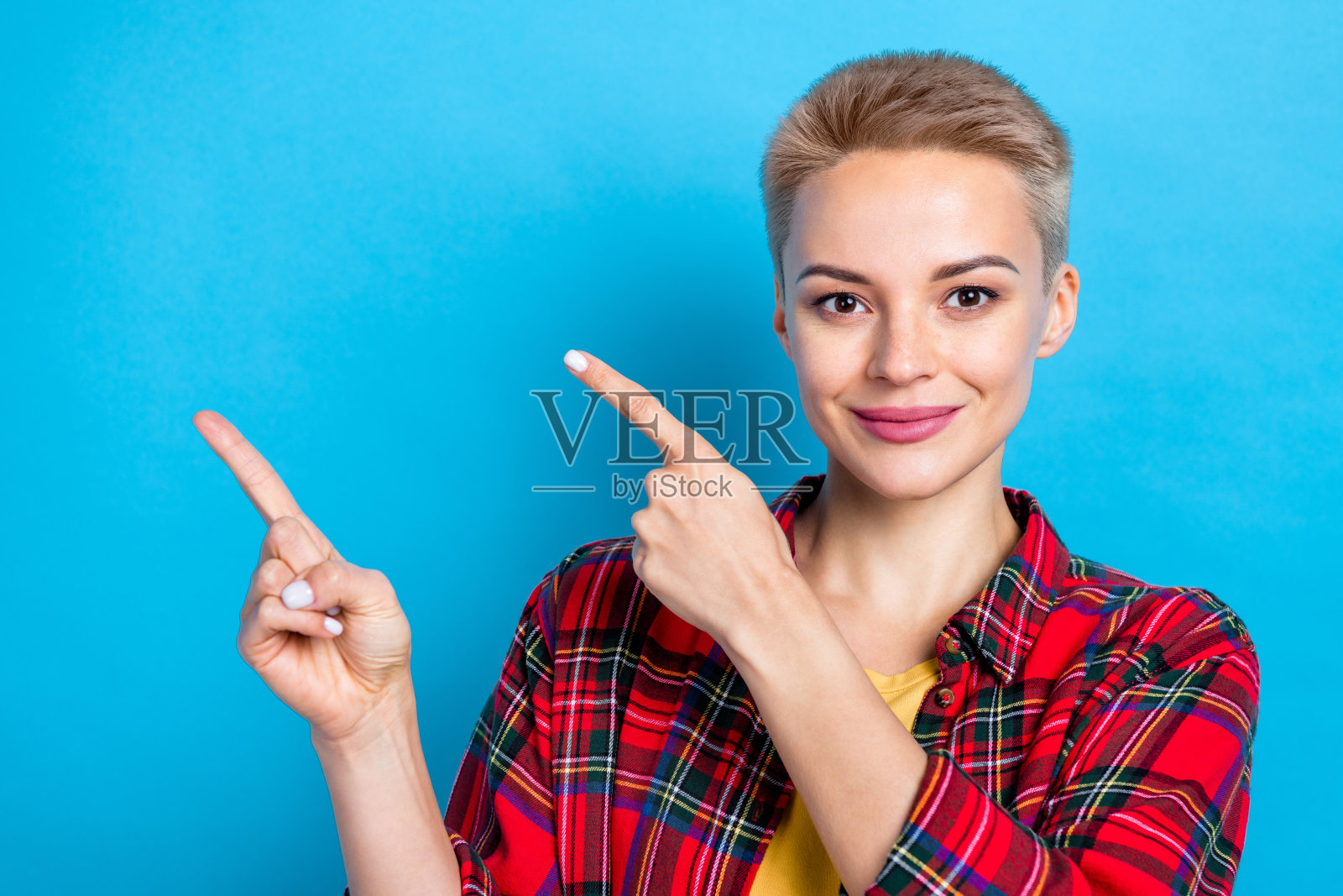 照片肖像金发短发女子穿红色格子衬衫直接手指空白的空间广告新课程孤立在蓝色的背景照片摄影图片