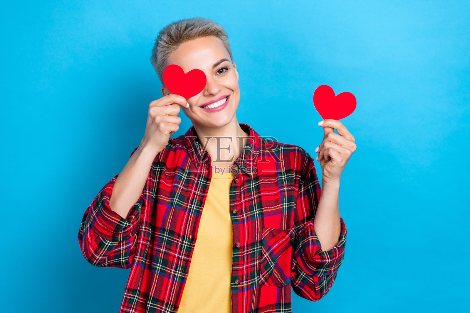 肖像乐观华丽的女人与短头发穿格子衬衫眼睛覆盖红纸像孤立的蓝色背景照片摄影图片